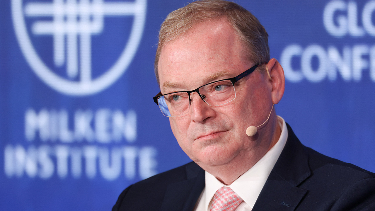 Kevin Hassett kalba spaudos konferencijoje fone matomas mikrofonas ir tamsus fonas